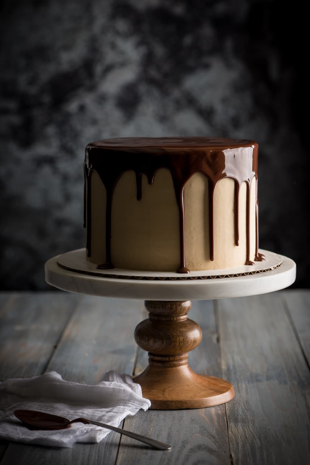 Chocolate peanut butter drip cake on a white cake stand